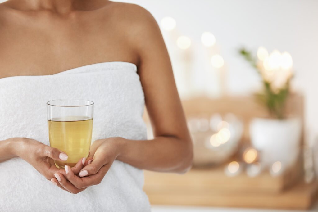 close up of young girl in towel holding glass with green tea in spa salon.
